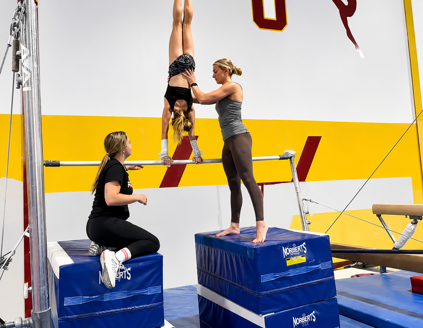 Coach spotting a gymnast on bars at H.U.G.S.