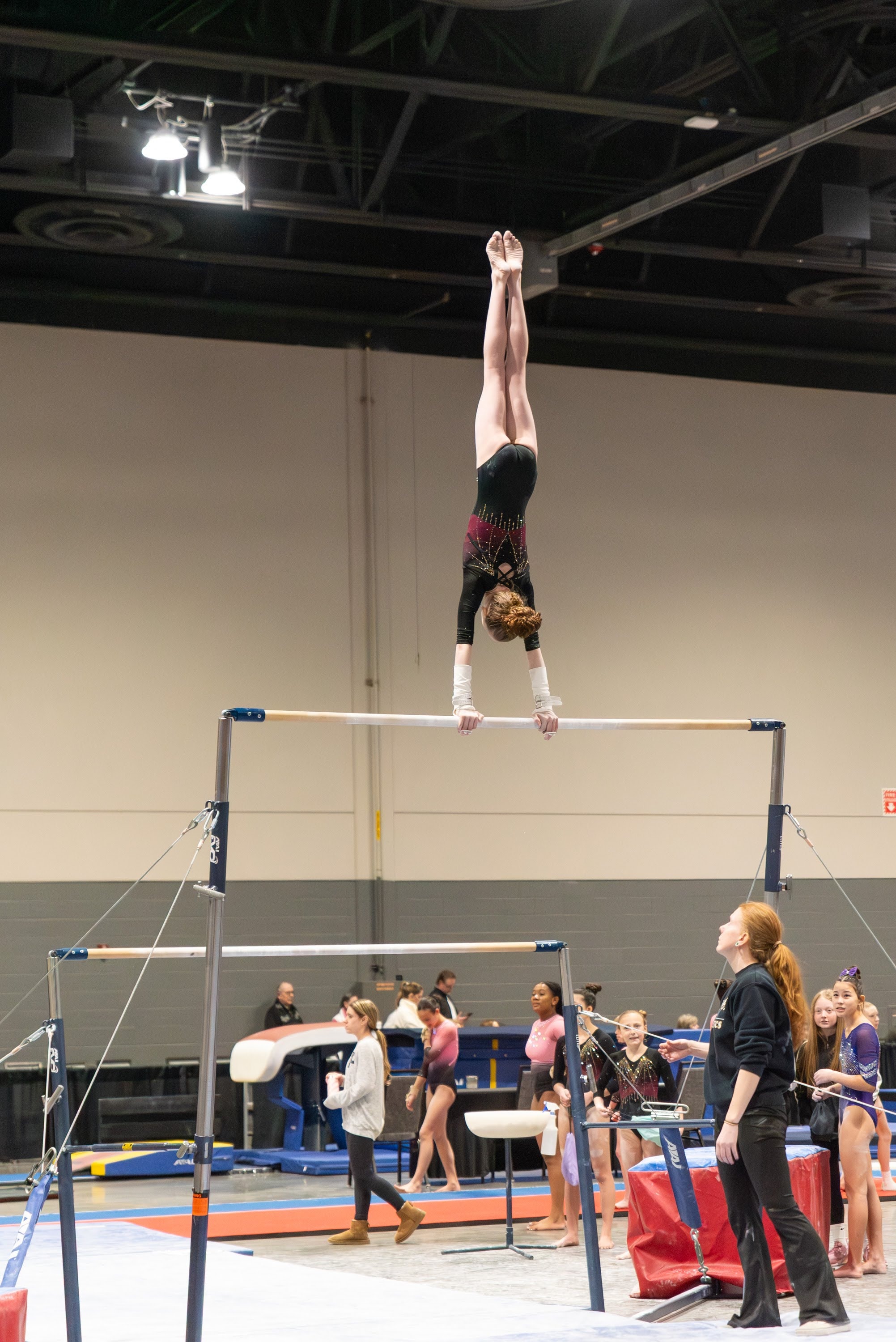 Gymnast performing a handstand on the uneven bars at a competition