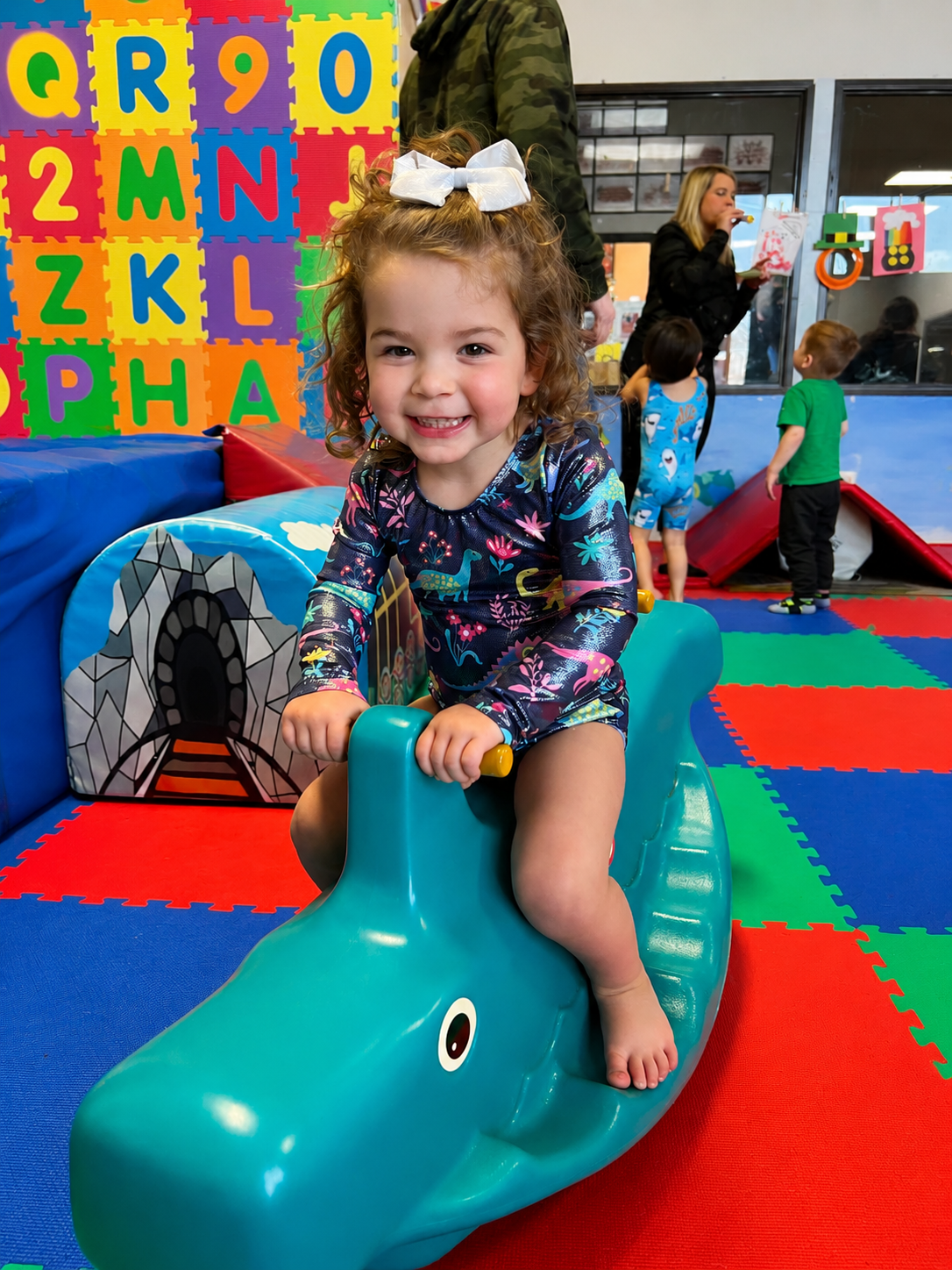Little girl smiling on the dolphin rocker in tots gym